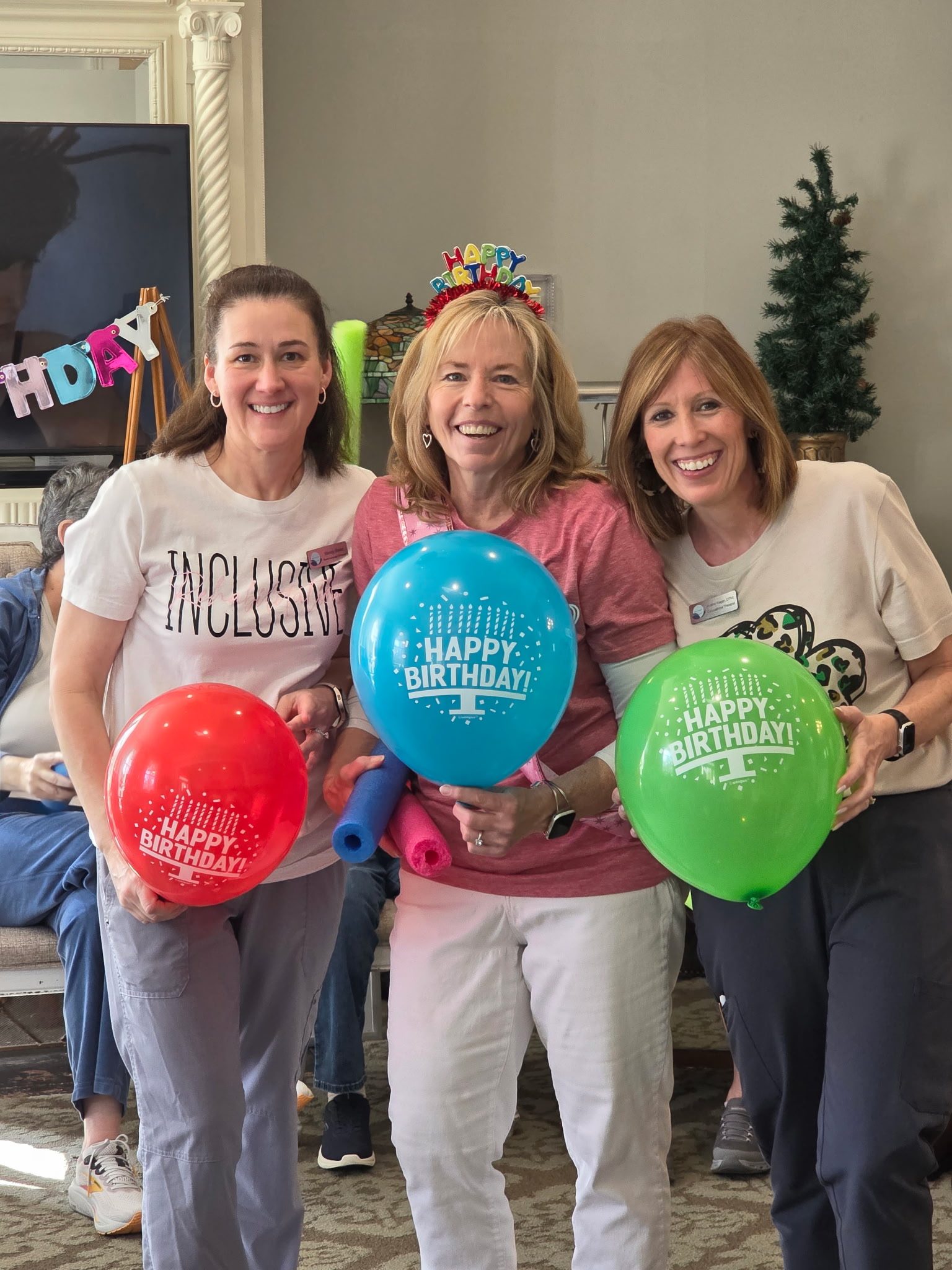 Three smiling staff members celebrating a birthday with balloons