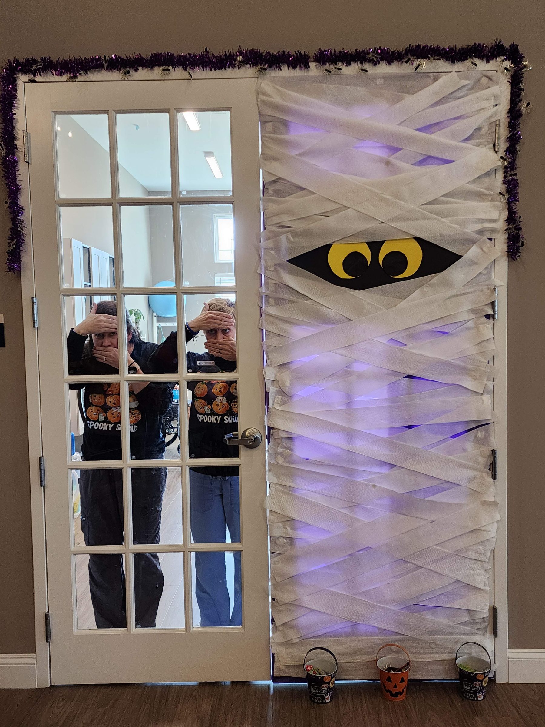 Two staff members peeking through a Halloween-decorated door