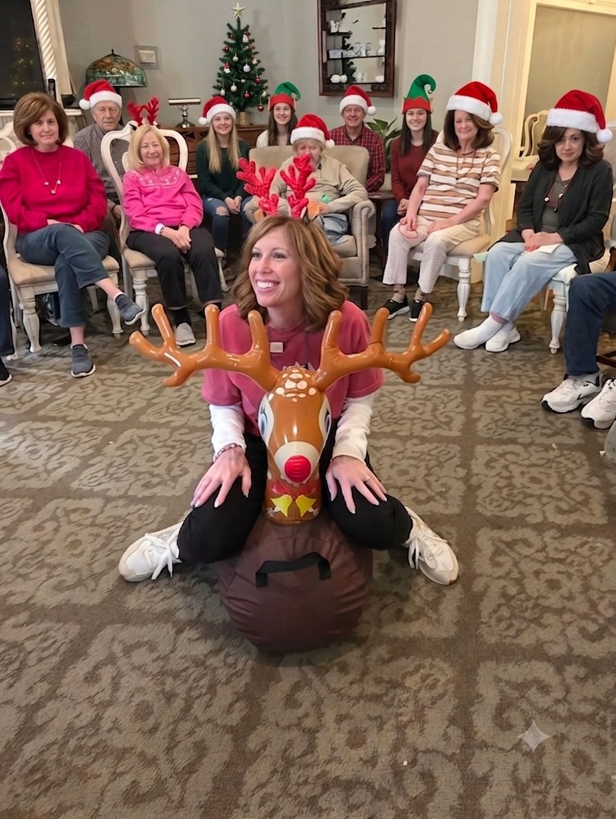 A staff member in a reindeer costume entertaining a group of residents and staff in Santa hats during the holidays